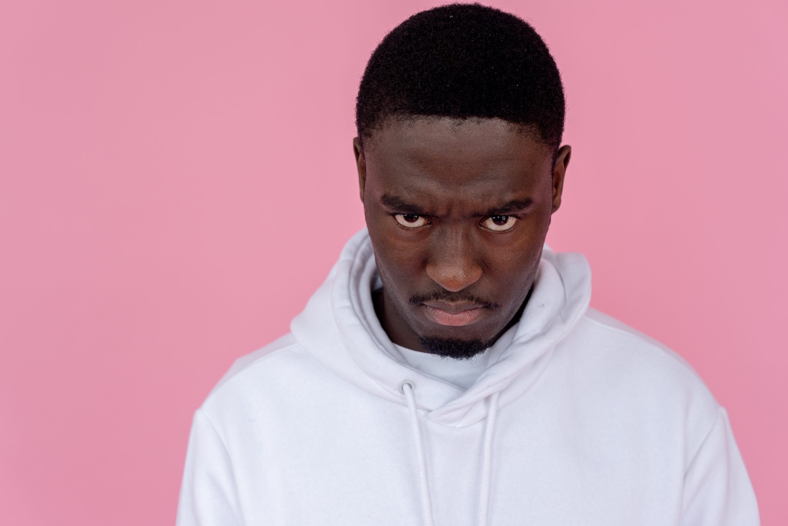 Photo by SHVETS production: https://www.pexels.com/photo/angry-black-man-in-hoodie-against-light-pink-background-6974921/